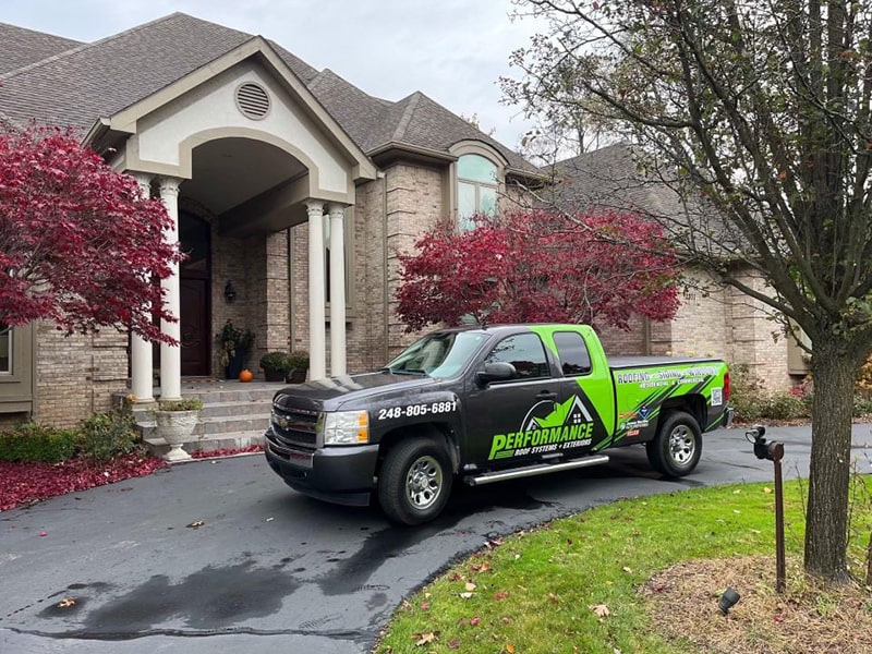 A house with black roof and brick style siding undergoing a roof inspection. Performance Roofing and Siding truck in front of the house in Michigan.