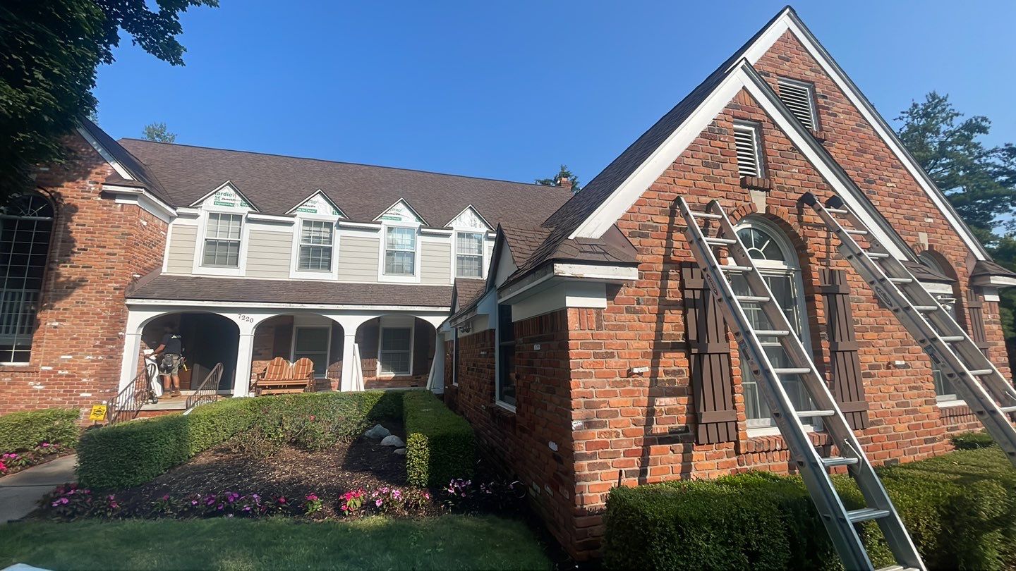 A brick house with dormer windows and a ladder against the facade by Performance Roofing and Siding.