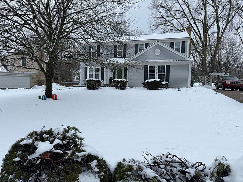 Two-story house with snow-covered yard and leafless trees.