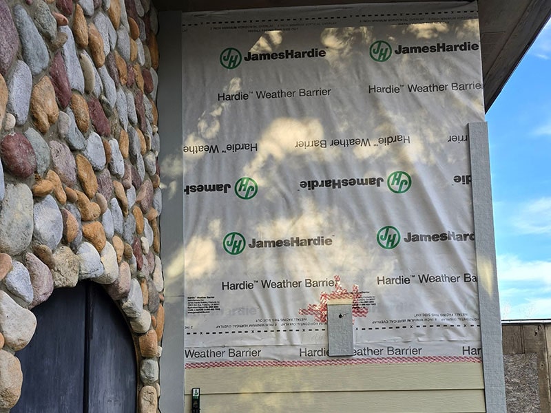 House wall with exposed weather barrier by James Hardie next to stone cladding.