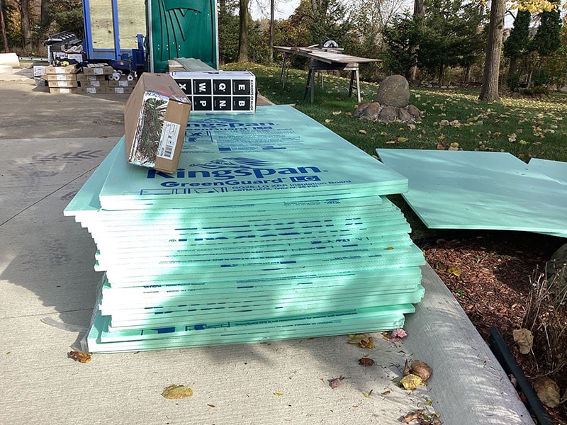 Stack of green foam insulation boards on a concrete surface outdoors by Performance Roofing and Siding.