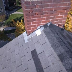 Roof with gray asphalt shingles, red brick chimney and metal flashing in a process of roof repair in Michigan