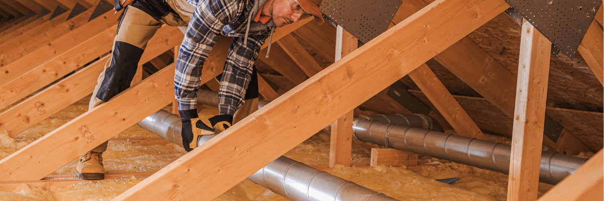 Technician inspecting ductwork and insulation for attic ventilation by Performance Roofing and Siding