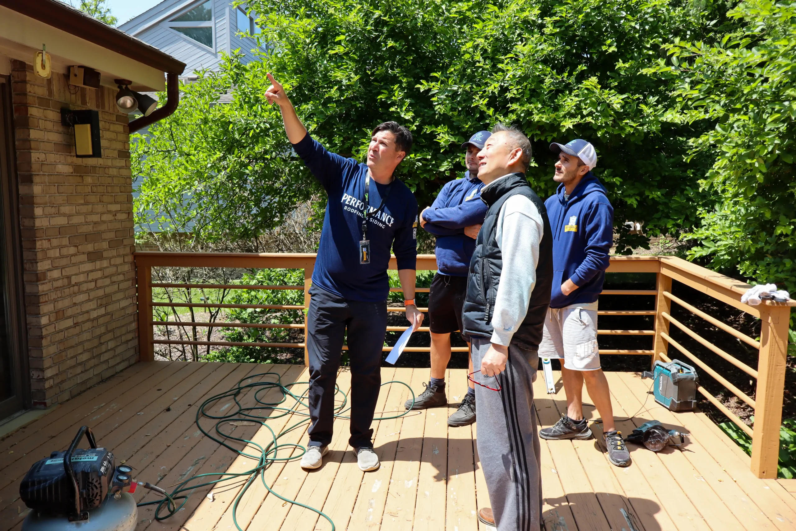 Performance Roofing & Siding team members meeting with a homeowner on a deck, pointing out details on the roof and discussing follow-up support after a roof inspection in Pontiac, MI.