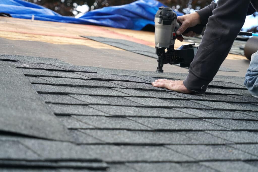 handyman using nail gun to install shingle to repair roof