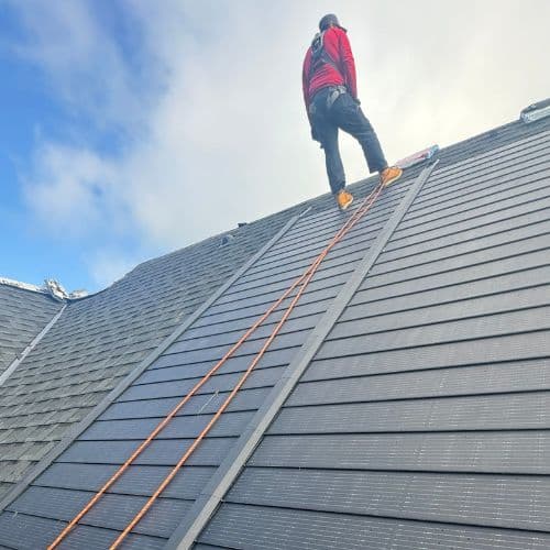 Roofer standing on a steep slope roof using safety gear during installation.