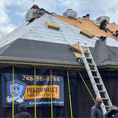 Roofing crew installing steep roof with Performance Roofing and Siding banner visible on house.