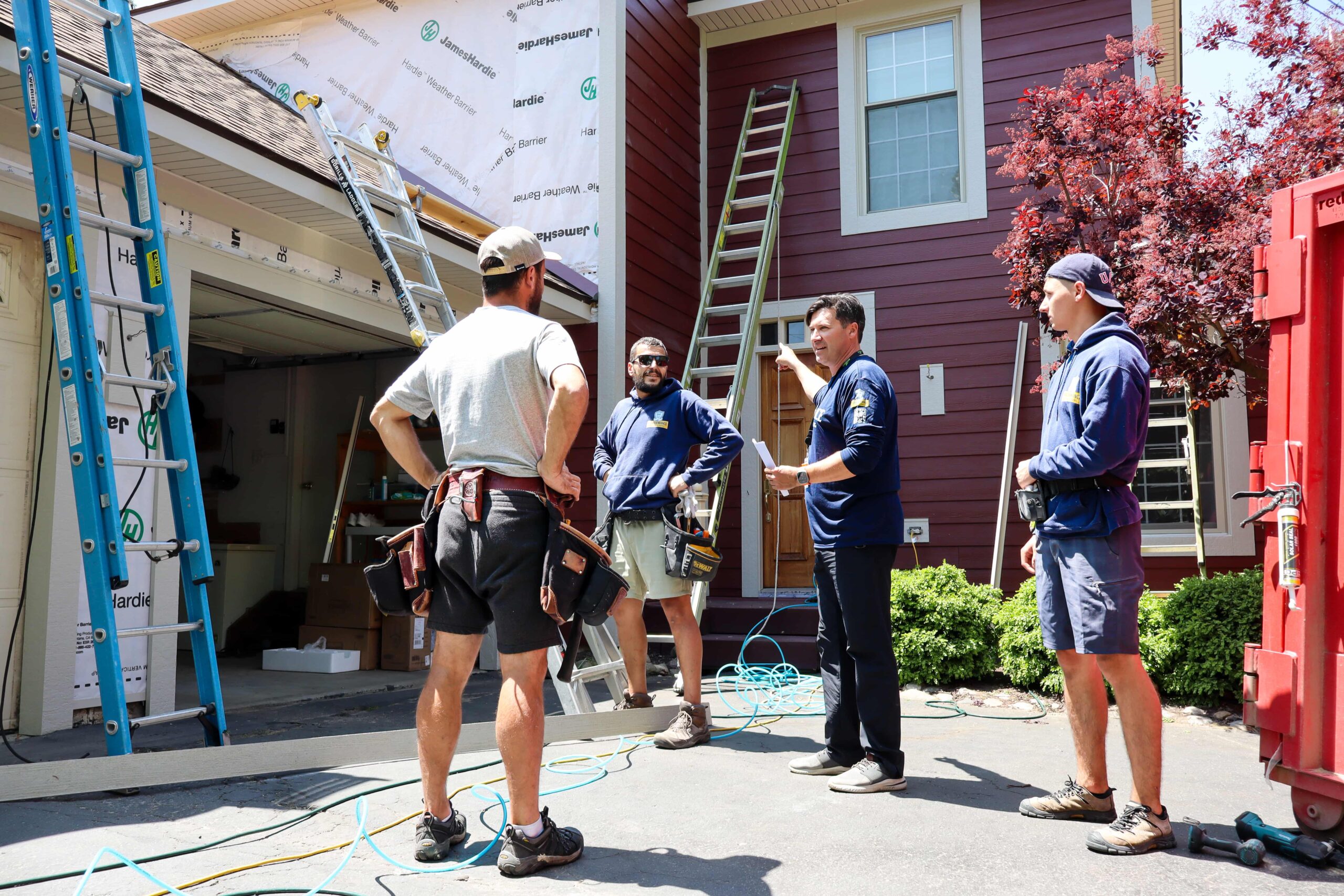 A Performance Roofing and Siding project manager discussing a siding installation with his crew at a residential job site.
