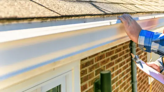 Professional inspector checking aluminum gutters for maintenance and repairs with clipboard in hand by Performance Roofing & Siding
