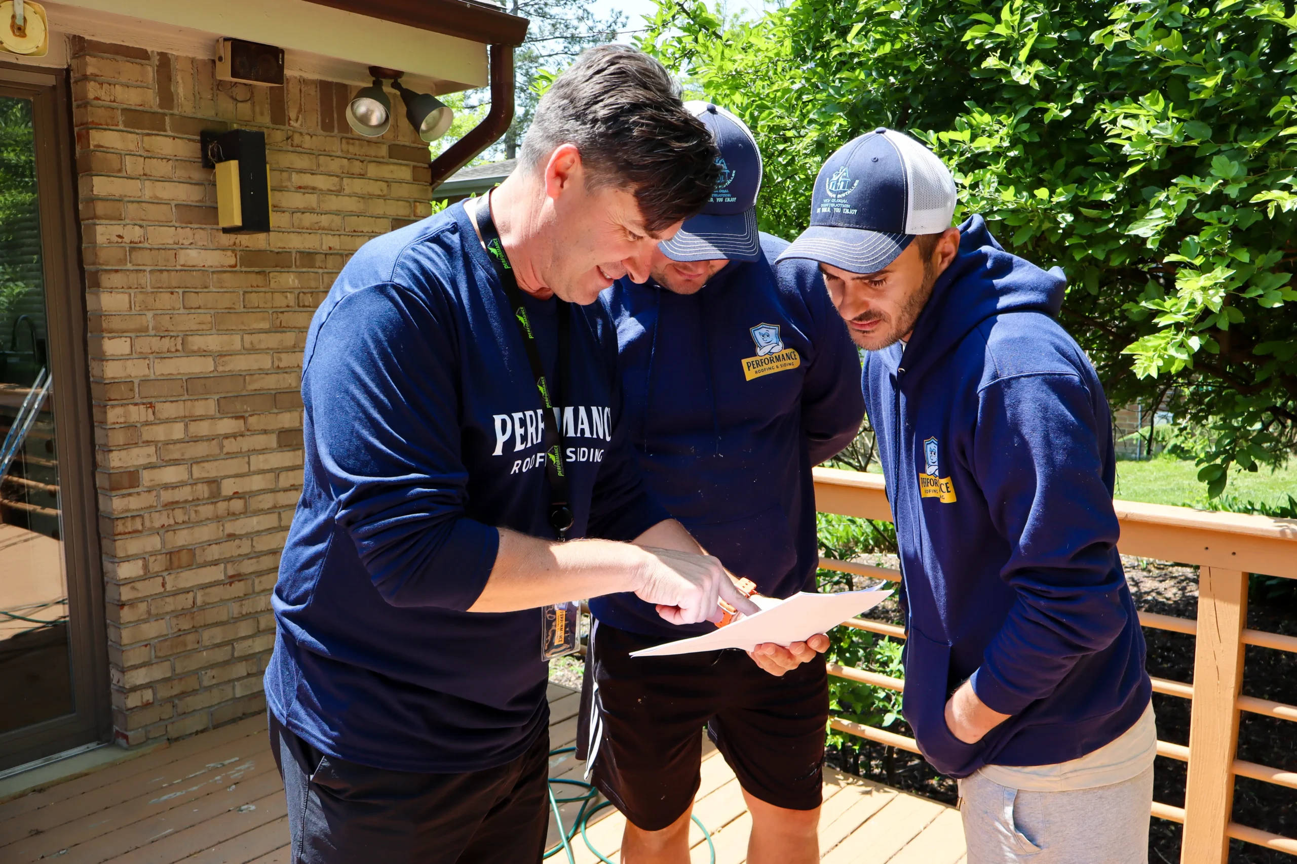 A Performance Roofing and Siding project manager discussing a siding installation with his crew at a residential job site.