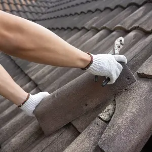 Gloved hands using a tool to replace a damaged roof tile during roof repair service by Performance Roofing & Siding
