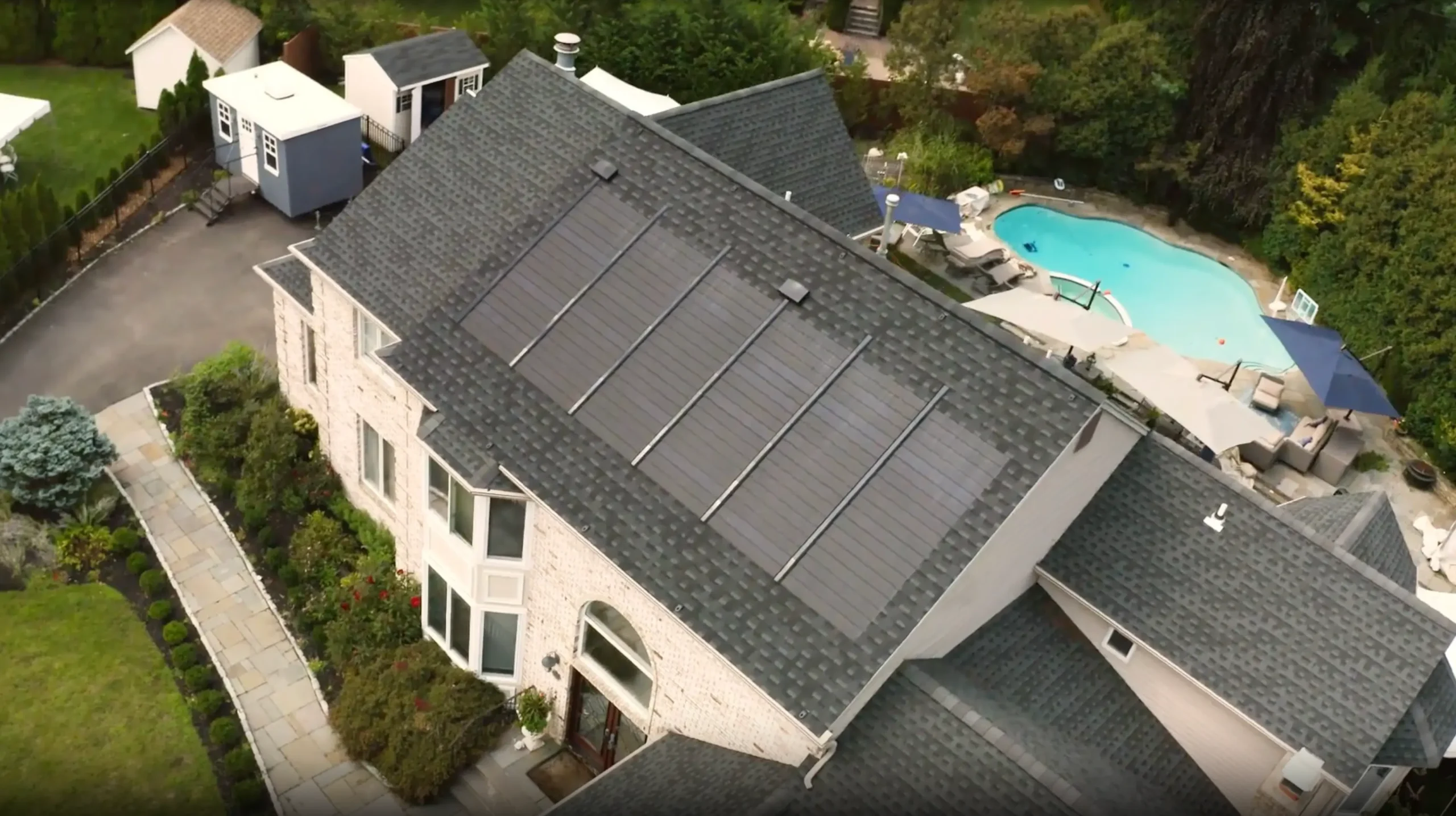 Aerial view of a house with Performance Roofing and Siding solar shingles installed on the roof next to backyard pool