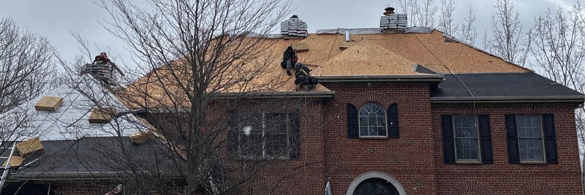 Full view of steep slope roof under construction with roofers working on decking.