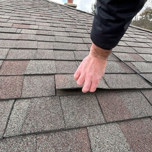 A close inspection reveals a damaged and flimsy asphalt shingle on an older roof.